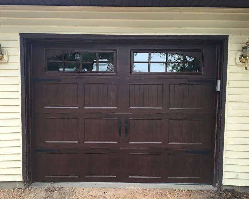 Dark walnut carriage-style single garage door with arched windows on a home with cream siding
